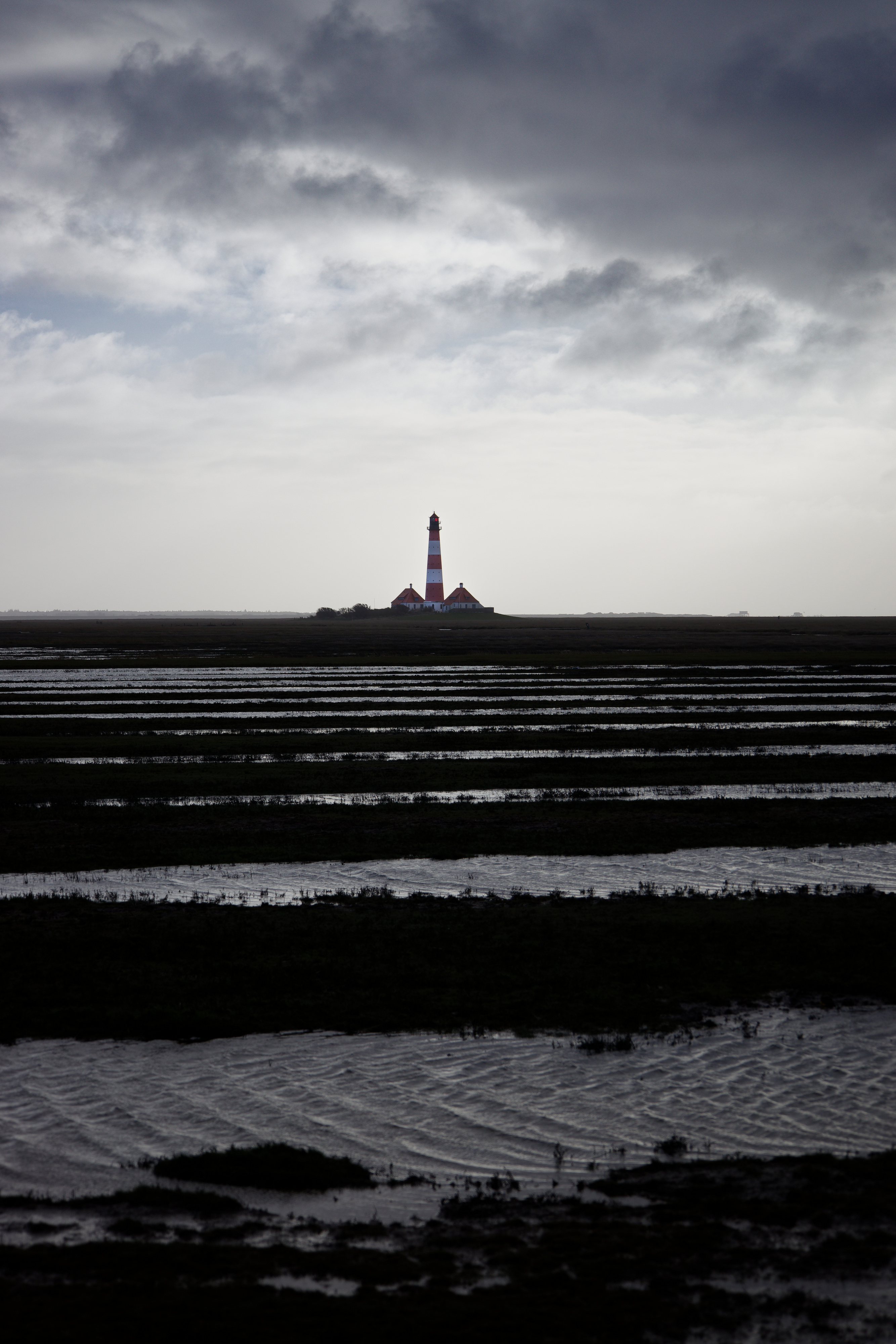 Der Leuchtturm Westerheversand steht in der Ferne. Im Vordergrund ist das Wattmeer.