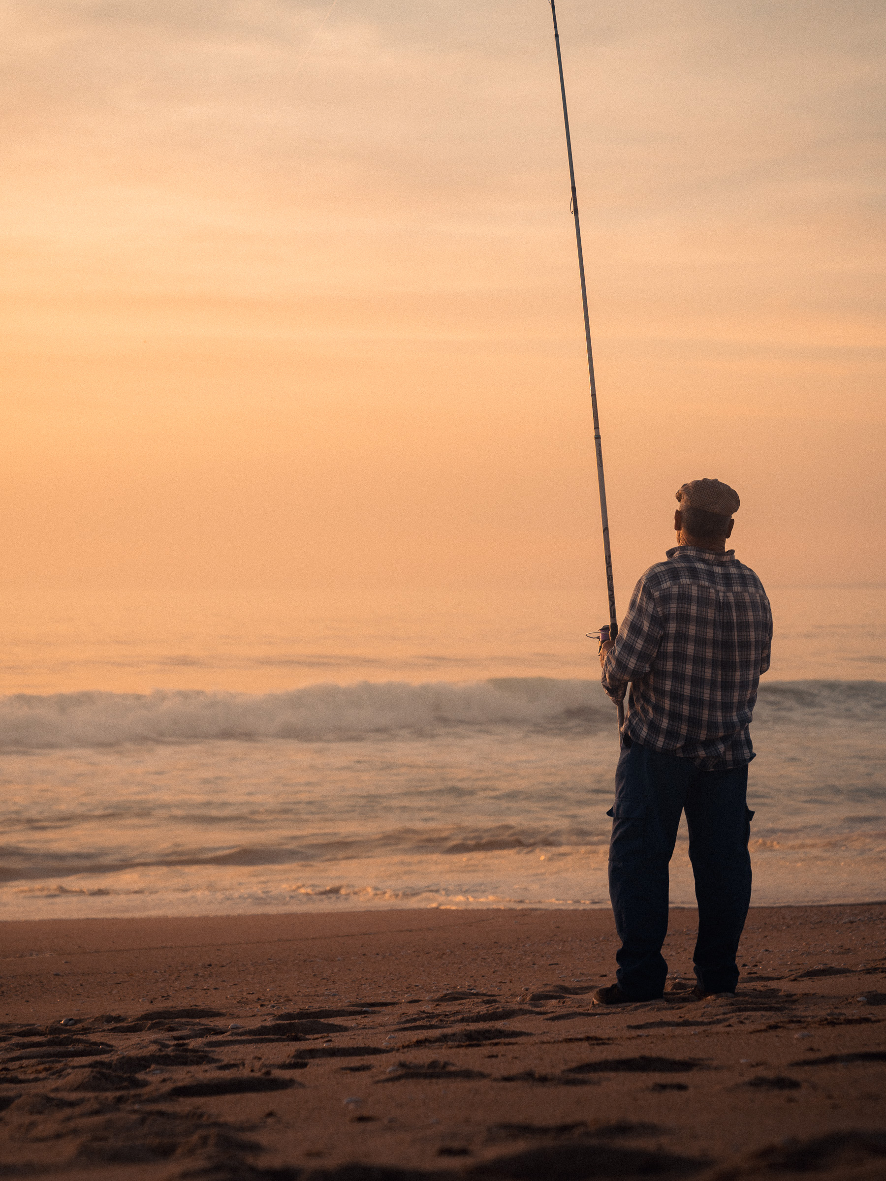 Ein Angler steht am Meer und schaut in den Sonnenuntergang